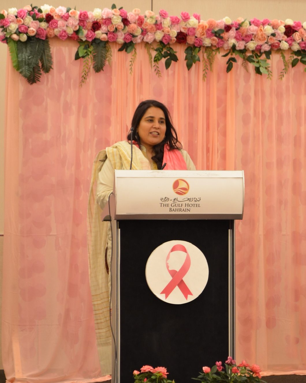 Shahmeen Islam speaking at a podium with a pink ribbon